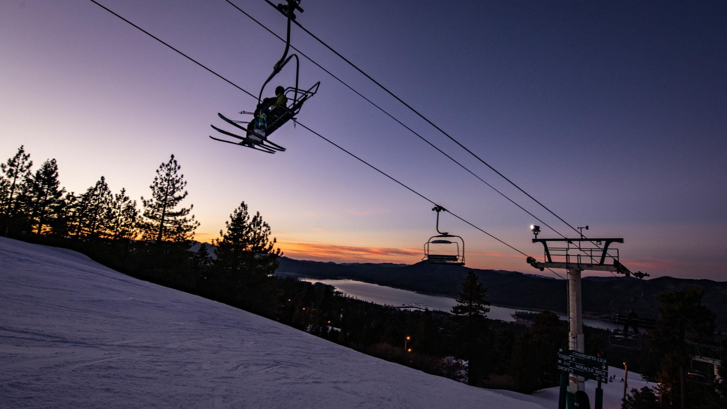 Two skiers on a chairlift during the evening.