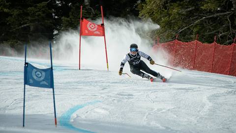 A teen skier carving down a Snow Summit race course weaving in and out of red and blue race gates on a sunny day.