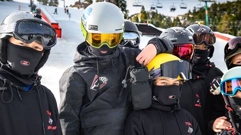 A group of Team Bear athletes in their black with Bear Mountain logo uniforms, snow helmets, and goggles in the terrain park of Bear Mountain.