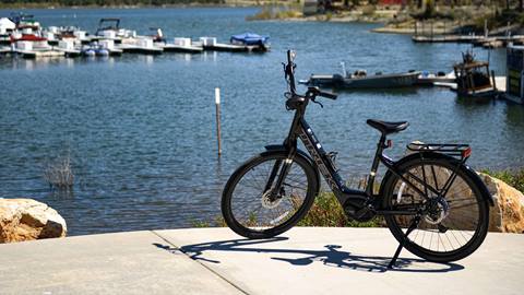 Black Trek eBike rental with the bike kick stand down in front of a park area with Big Bear Lake and boats docked in the marina.