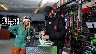 Girl waiting for her snowboard to be repaired by a technician.