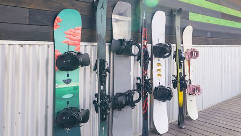 Side angle of three demo skis and four demo snowboards leaned up against a building at Snow Summit.