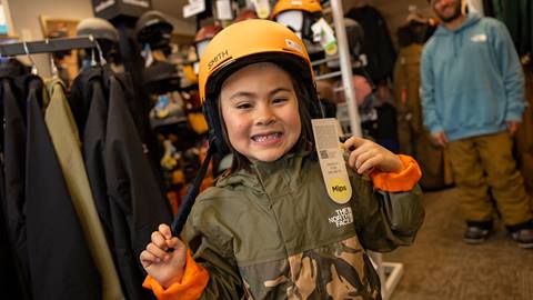 young child snowboarder trying on a new helmet in the sports shop