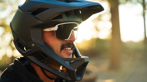 Close up head shot of an adult in a black full face mountain bike helmet with white Smith sunglasses.