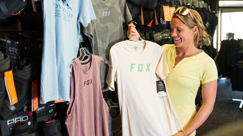 female shopper holding up a fox head branded tan tshirt, looking at it, smiling