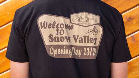 Black shirt with a brown and tan logo that says welcome to snow valley, opening day 23/24
