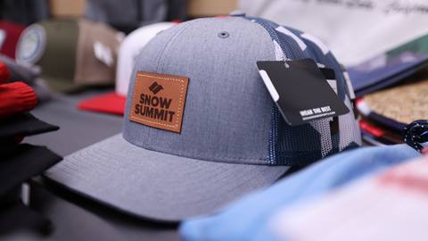 Snow Summit brown leather logo patch hat displayed on table with varying hats in the background.
