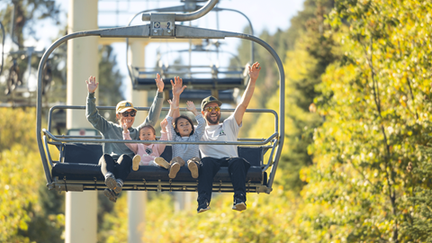 Family of 4 riding the scenic sky chair at snow summit in the fall with yellow leaves in the background