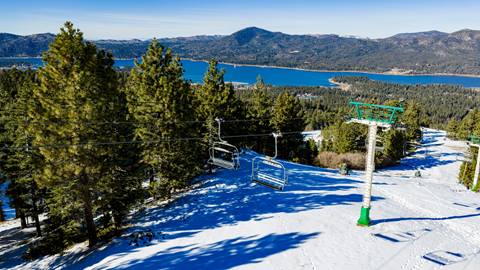A drone image looking at Big Bear Lake, from Snow Summit, with snow on the slopes and a chairlift in plain sight.