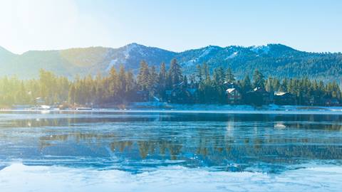 A scenic shot of Big Bear Lake on a blue sky day with the snowy slopes of Snow Summit Ski Resort in the distance.