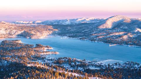 Morning sunrise glow over Big Bear Lake with the lake and white snow dusted mountains in the distance.