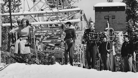 An old black and white photo of an adult on a single person chairlift during the winter time.