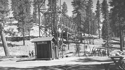 Black and white photo of an original single person chairlift during a summer day at Snow Valley with adults unloading and loading onto the chairlift.