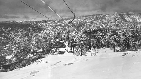 Black and white photo of a sunny winter day with a single ski chairlift at Snow Valley, and panoramic view of the San Gabriel Mountains.