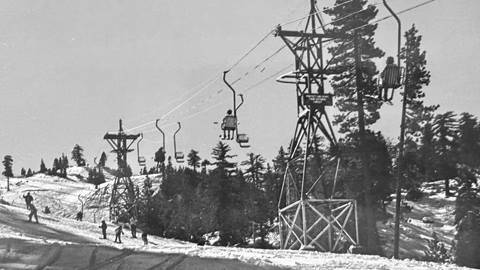 Skiers on a white snowy trail and skiers riding up the single person chairlift at Snow Valley.