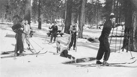 Six adults posing for the camera while on the snow and in cold weather clothing wearing skis.