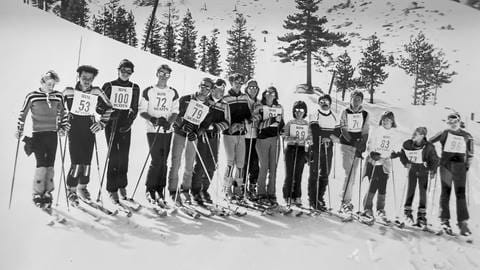 A group of 15 skiers, most wearing a white bib with the words Rim Scots, posing for the camera while on their skis on the slopes of Snow Valley