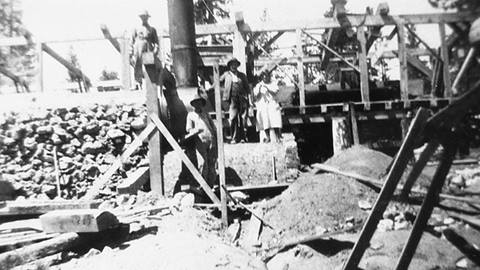 Four adults posing next to wood beams, rocks, and dirk while working at the Snow Valley construction site.
