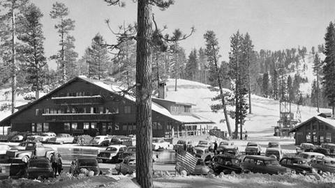 A highway view looking towards the base area and chalet building of Snow Valley with a parking lot full of cars.