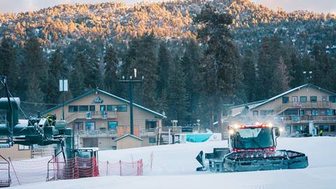 On the hill photo looking to the Snow Valley chalet buildings and base area, during a sunny morning as a snow cat is grooming the snow on the base area ski trails.