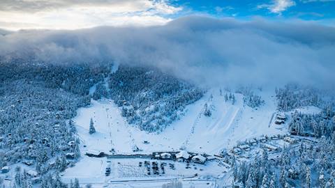 Drone image of a snowy Bear Mountain with blue skies and clouds hovering over the resort