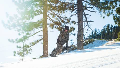 Snowboarder in military uniform sliding down the slopes on a sunny day