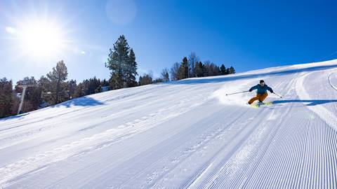 A skier riding down a freshly groomed corduroy trail at Snow Summit during a sunny blue sky winter day.