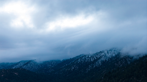 Fresh snow blanketing the pine trees and mountains at Big Bear Mountain Resort under a partly cloudy sky.