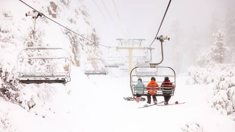 Three snowboarders on a chairlift during a cloudy snowy day