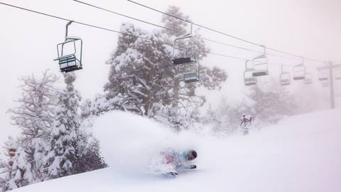 Snowboarder on a snow day carving in powder under a chairlift. 