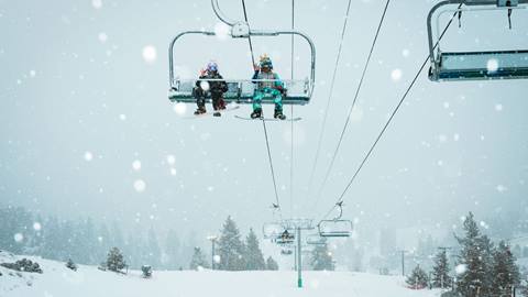 Two snowboarders on the chairlift enjoying new snowfall on a cloudy snow day