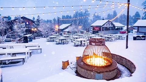 The base area at Snow Summit during a snow storm with the walkways, a fire pit, tables, and chairs covered with a fresh coat of snow.