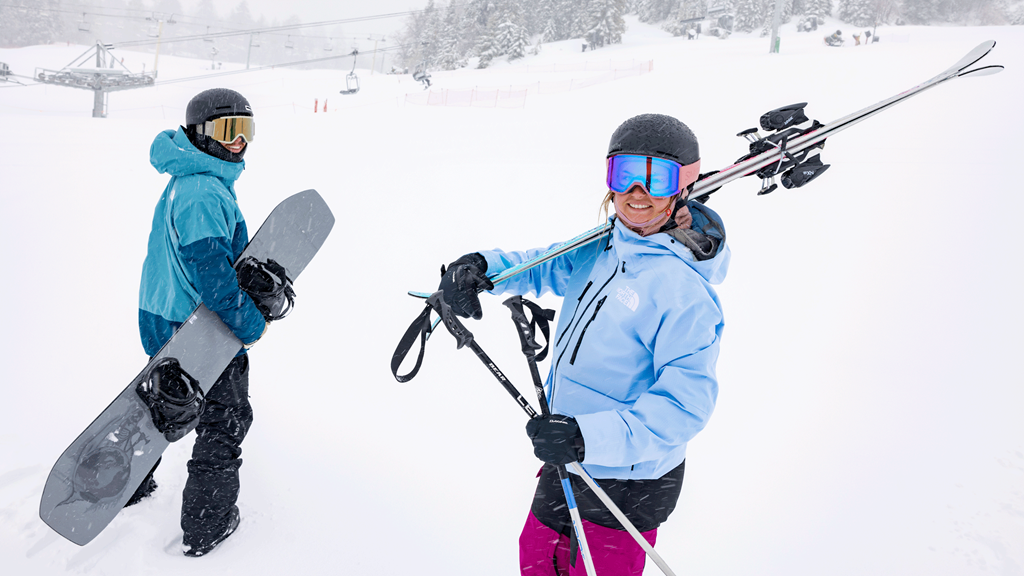 Skier and snowboarder with their gear walking towards the ski slope