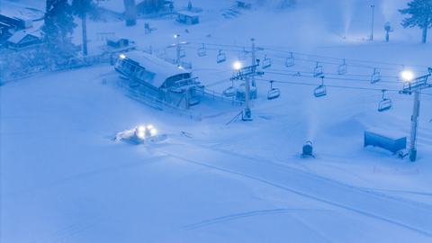 An arial drone image of Snow Summit's Chair 1 during morning with snow guns blowing man-made snow and a snow cat grooming the trail to fresh corduroy perfection.