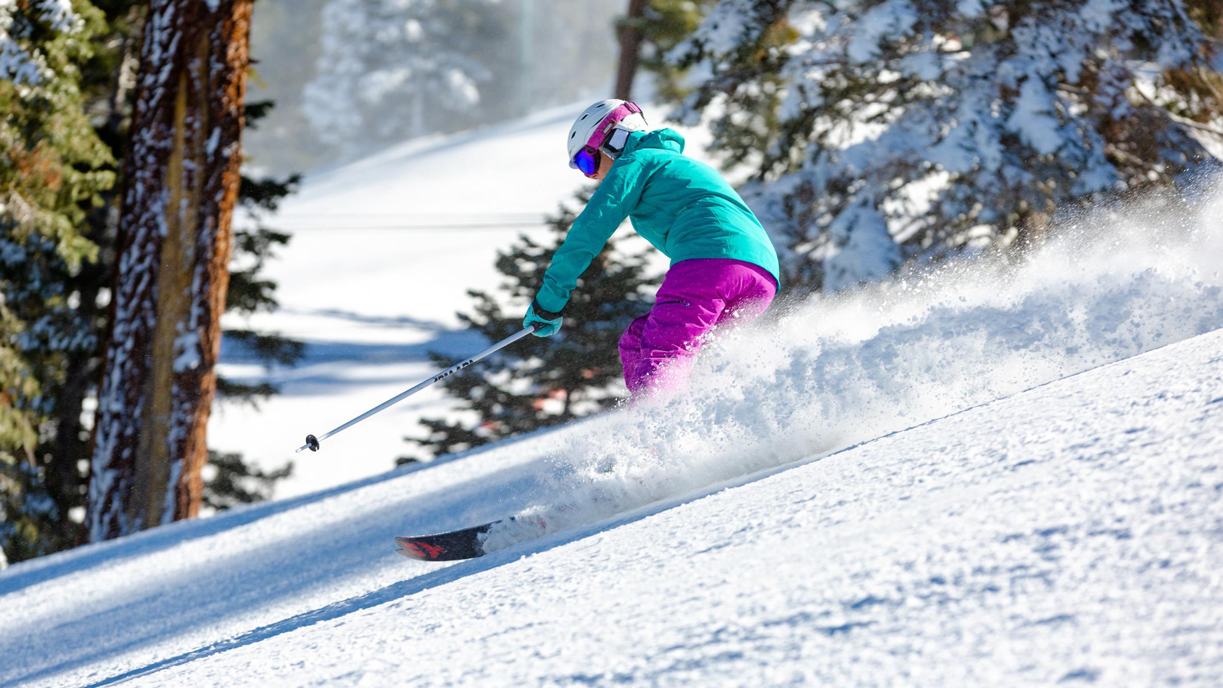 Skier wearing bright green jacket and purple pants going down the ski slope.
