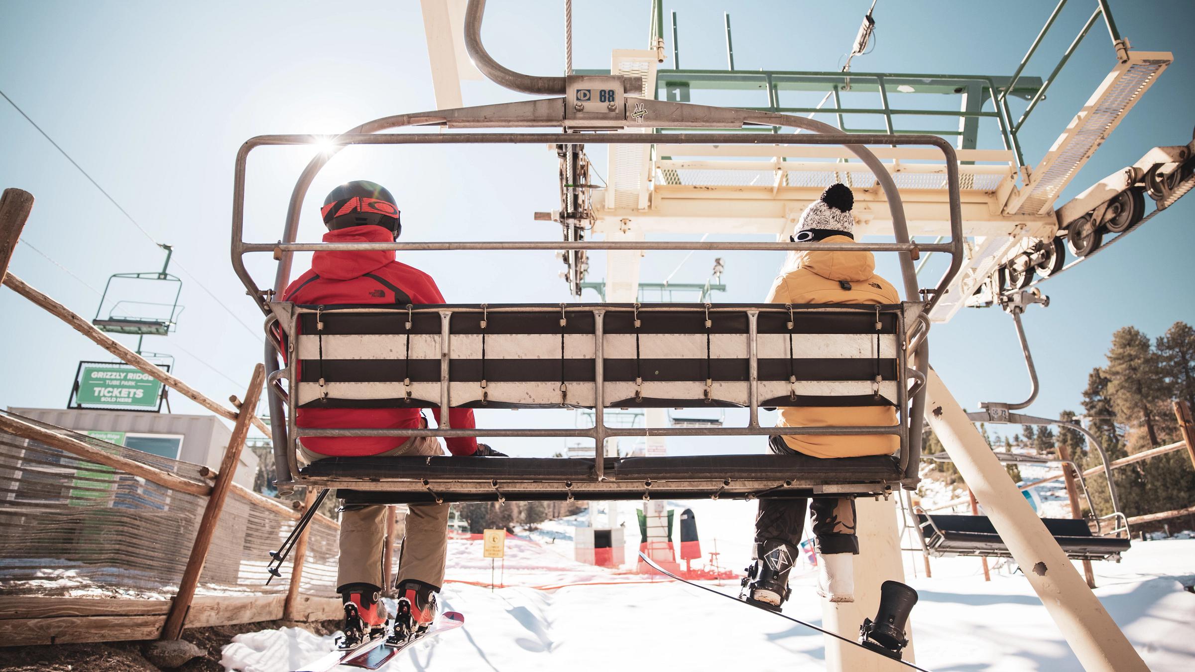 A skier and snowboarder going up on a chairlift.