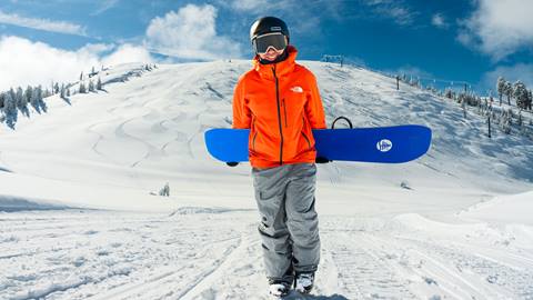 Smiling snowboarder holding board behind back while at the base of Snow Valley's Slide Peak
