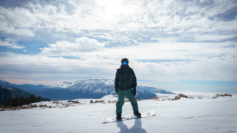 Snowboarder standing at the top of Snow Valley on their snowboard with a great view in the background of snowy mountain tops and clouds