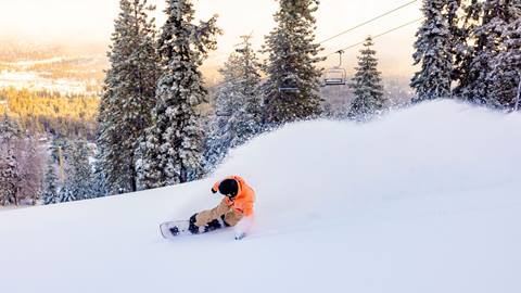Snowboarder in orange jacket on a powder day slashing and fresh snow is spraying in the air