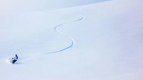 Snowboarder riding in fresh powder with a single line s track behind