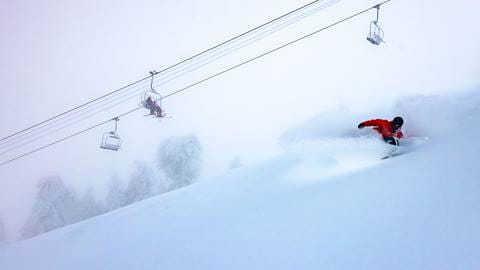 Snowboarder in red jacket under the chairlift carving through fresh powder
