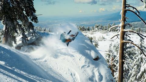 Snowboarder doing a slash on a rock feature with snow covering it