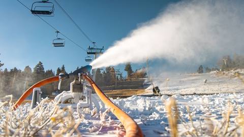 Snowmaking guns under chairlift blowing snow into the air and ski hill.