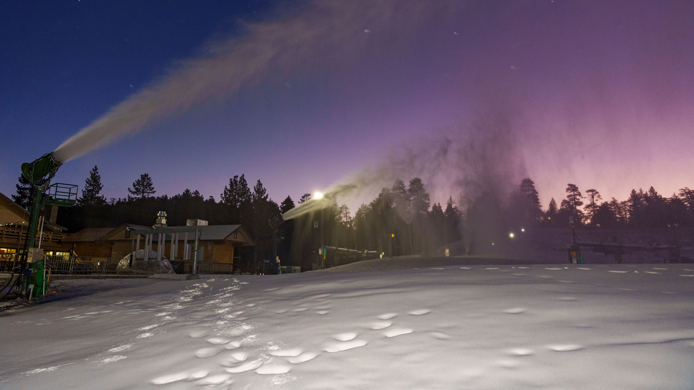 A winter mrning sunrise with a blue, pink, and purple clear sky and snow machine guns turned on at the base area of Snow Valley.