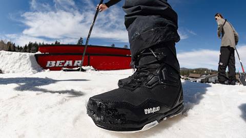 A close up of two Bear Mountain terrain park team members grooming a red terrain park features on-hill during a sunny winter day while wearing black Thirty-Two snowboard boots.