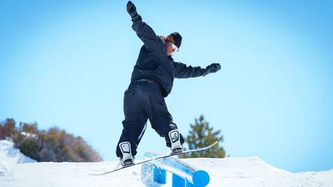 Snowboarder in all black front board sliding a down flat rail at Snow Valley