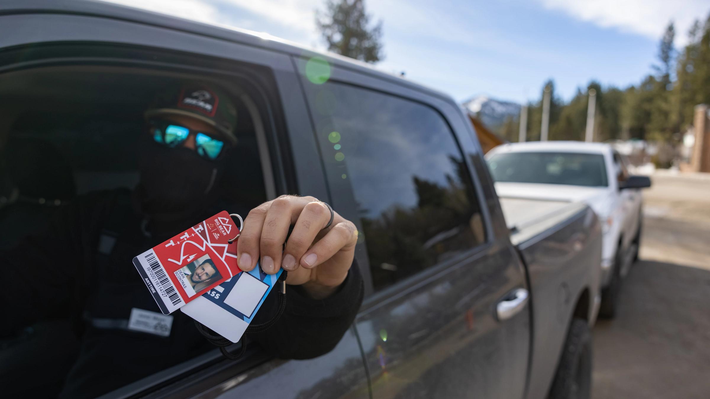 Guy holding out his season pass while sitting in a car