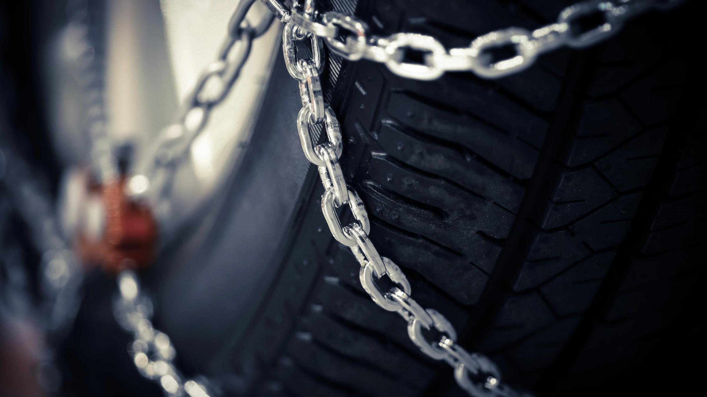 Horizontal detail shot of some new snow chains on a car's tire.