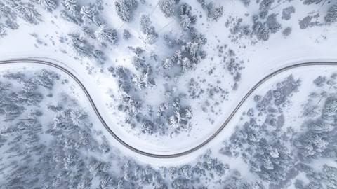 Drone view looking down to a windy road with alpine trees lining the highway and fresh snow after a winter storm.