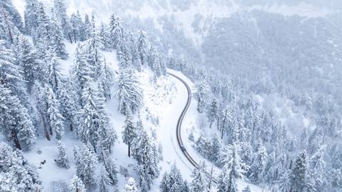 Ariel birds eye dron view of a road near Big Bear Lake with snow covering the highway and trees. 